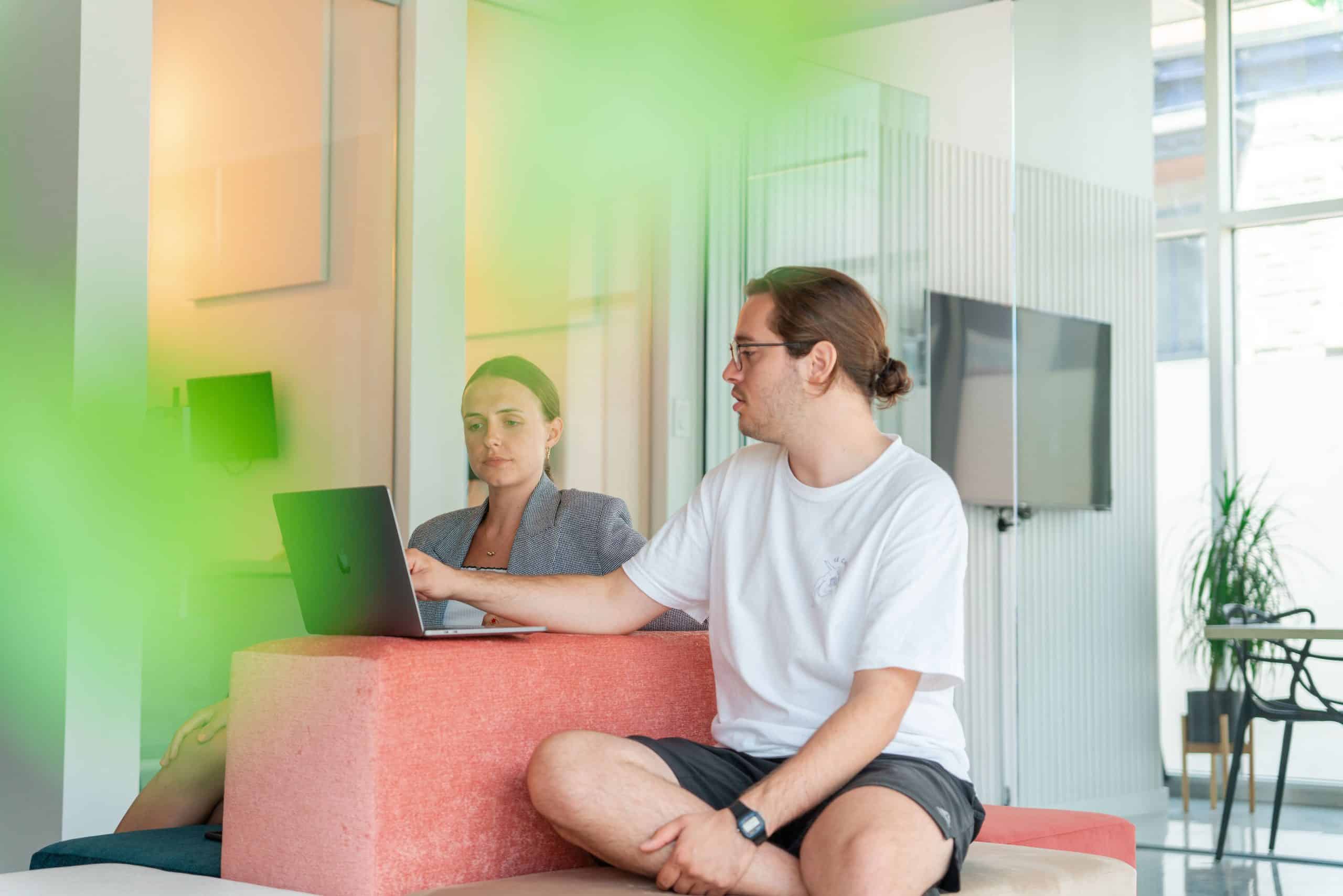 Un jeune homme et une femme qui travaillent dans une agence de marketing numérique discutent ensemble autour d'un ordinateur.